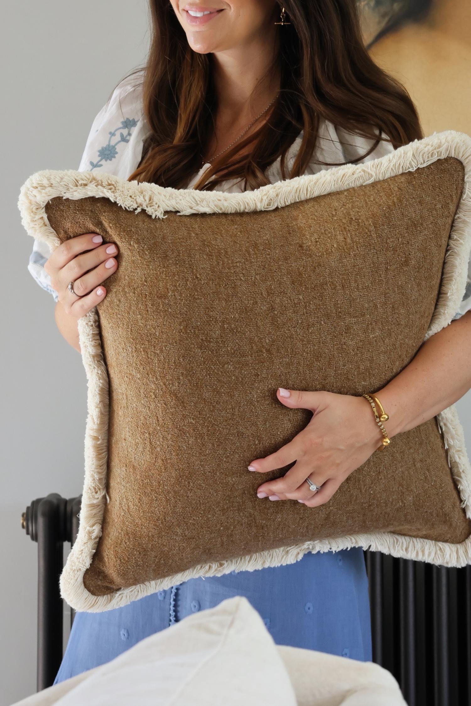 women holding textured brown cushion with beige fringe trim