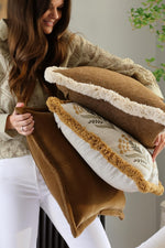 Woman holding three decorative cushions with a neutral background
