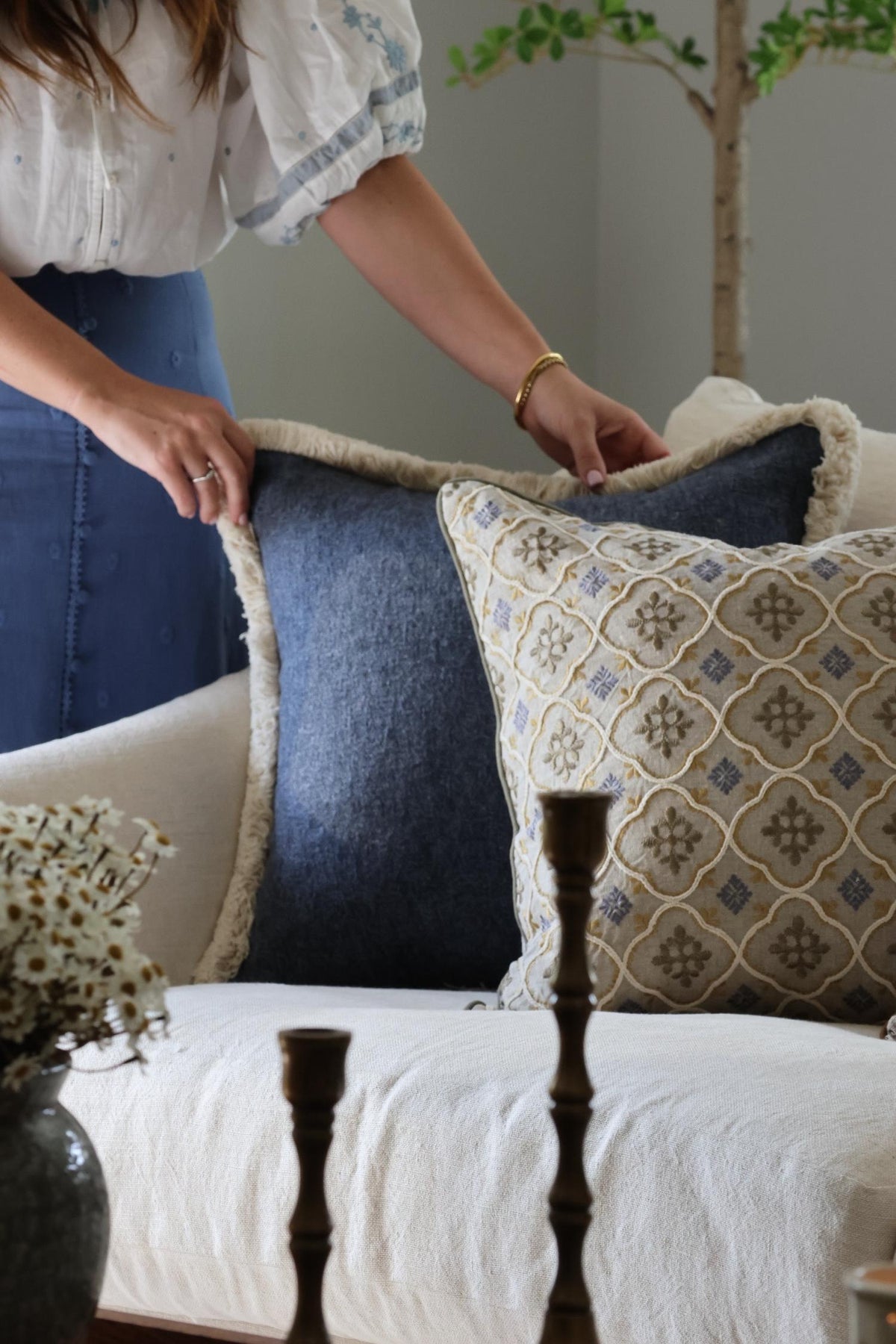 Person arranging decorative blue cushions on a sofa with a neutral background