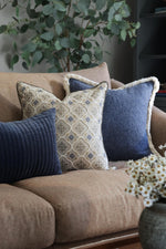 Decorative blue cushions on a brown sofa with a plant and vase in the background