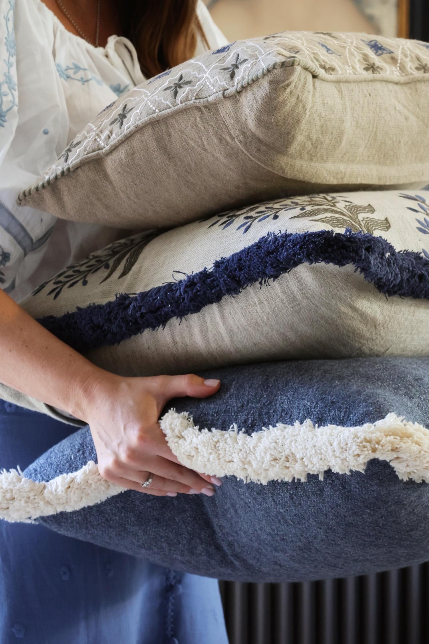 Person holding a stack of decorative blue cushions with intricate patterns