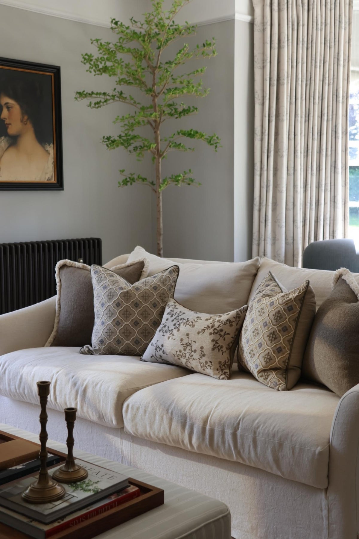 Living room with a beige sofa adorned with patterned cushions, a small tree, and a painting on the wall.