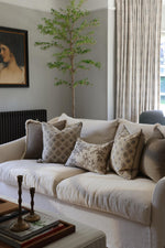 Living room with a beige sofa adorned with patterned cushions, a small tree, and a painting on the wall.
