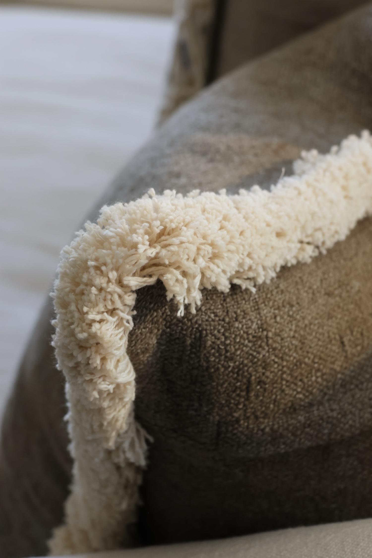 Close-up of a textured green cushion with a beige fringe trim on a blurred background