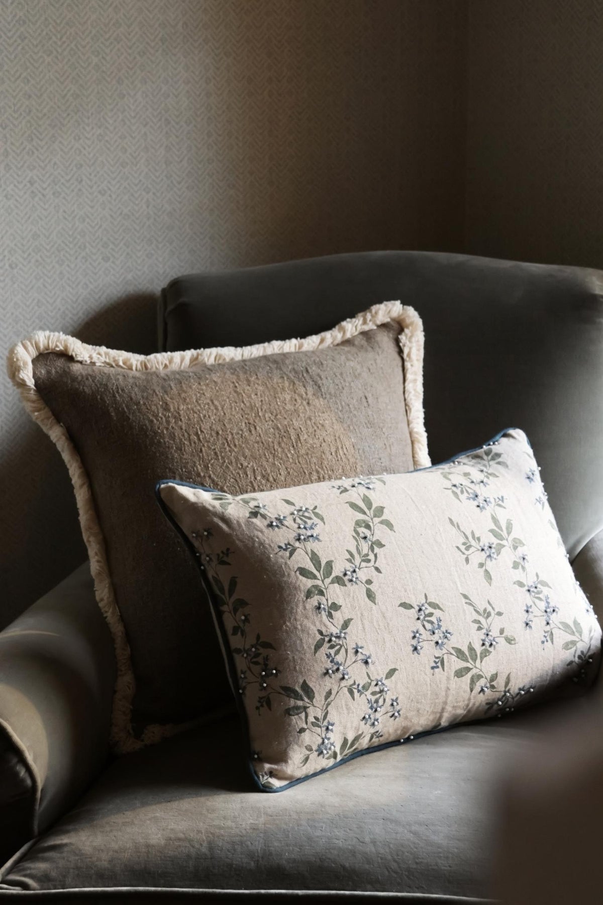 Two decorative cushions on a gray armchair against a neutral wall.