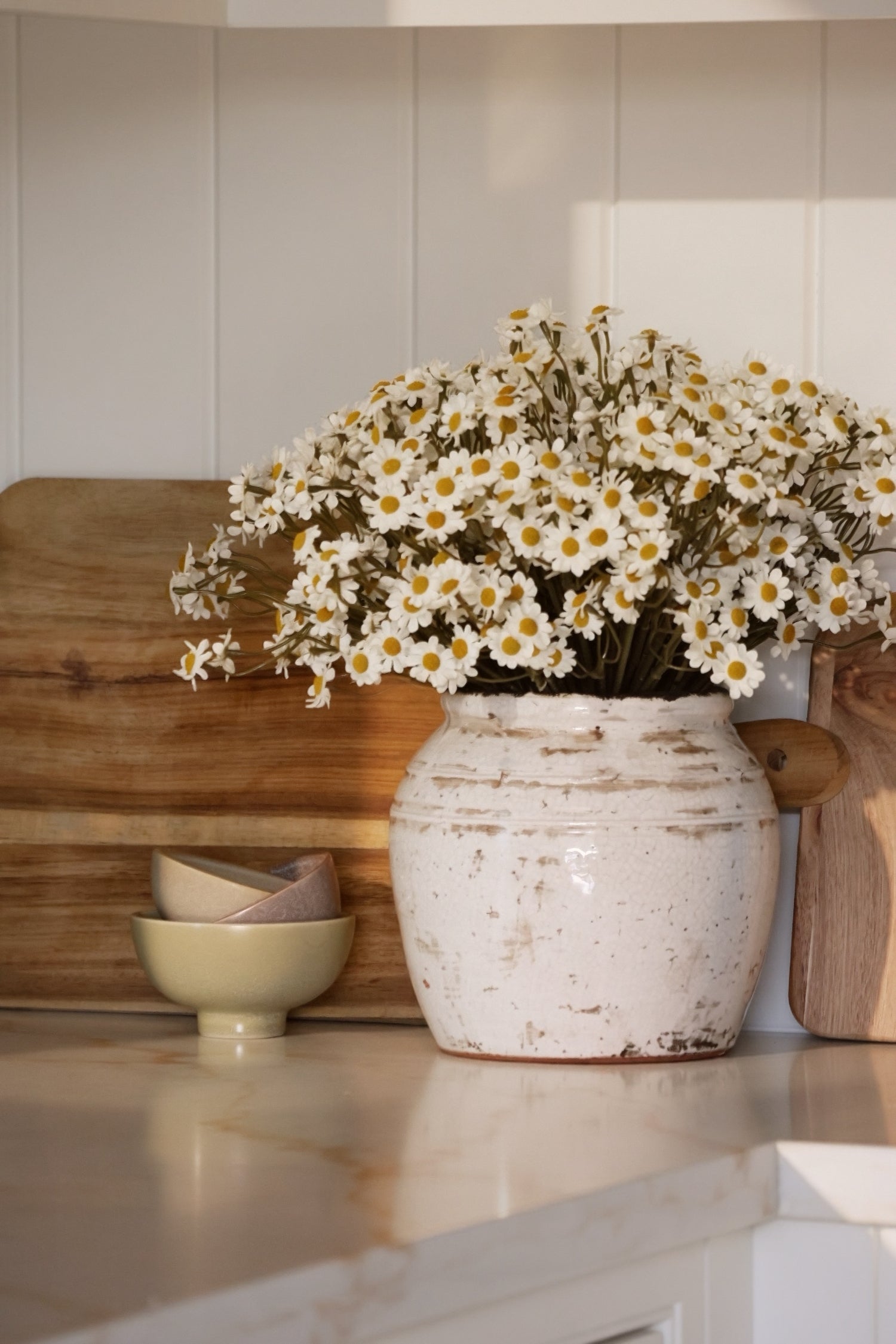 White vase with bunch of daisies on a kitchen counter