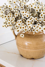 mustard ceramic vase with white daisy flowers on a marble surface