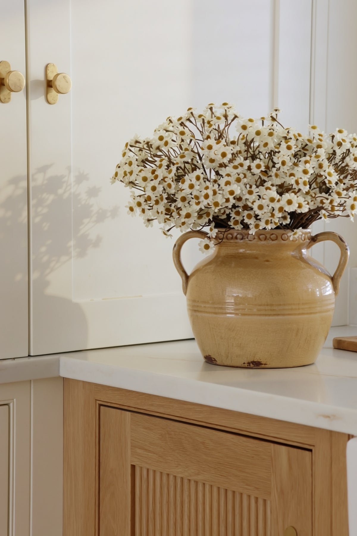 mustard ceramic vase with white daisy flowers on a kitchen counter