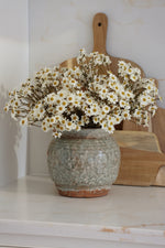 Vase with white daisy flowers on a marble surface with a wooden cutting board in the background