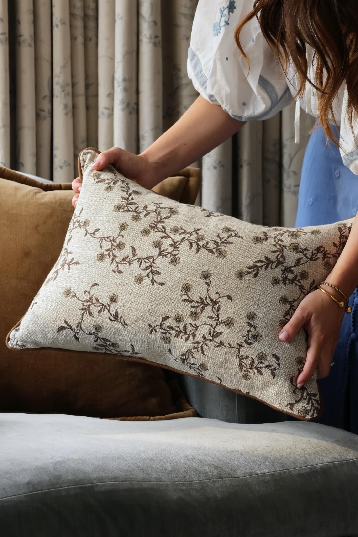 Person holding a floral-patterned linen cushion in a home setting
