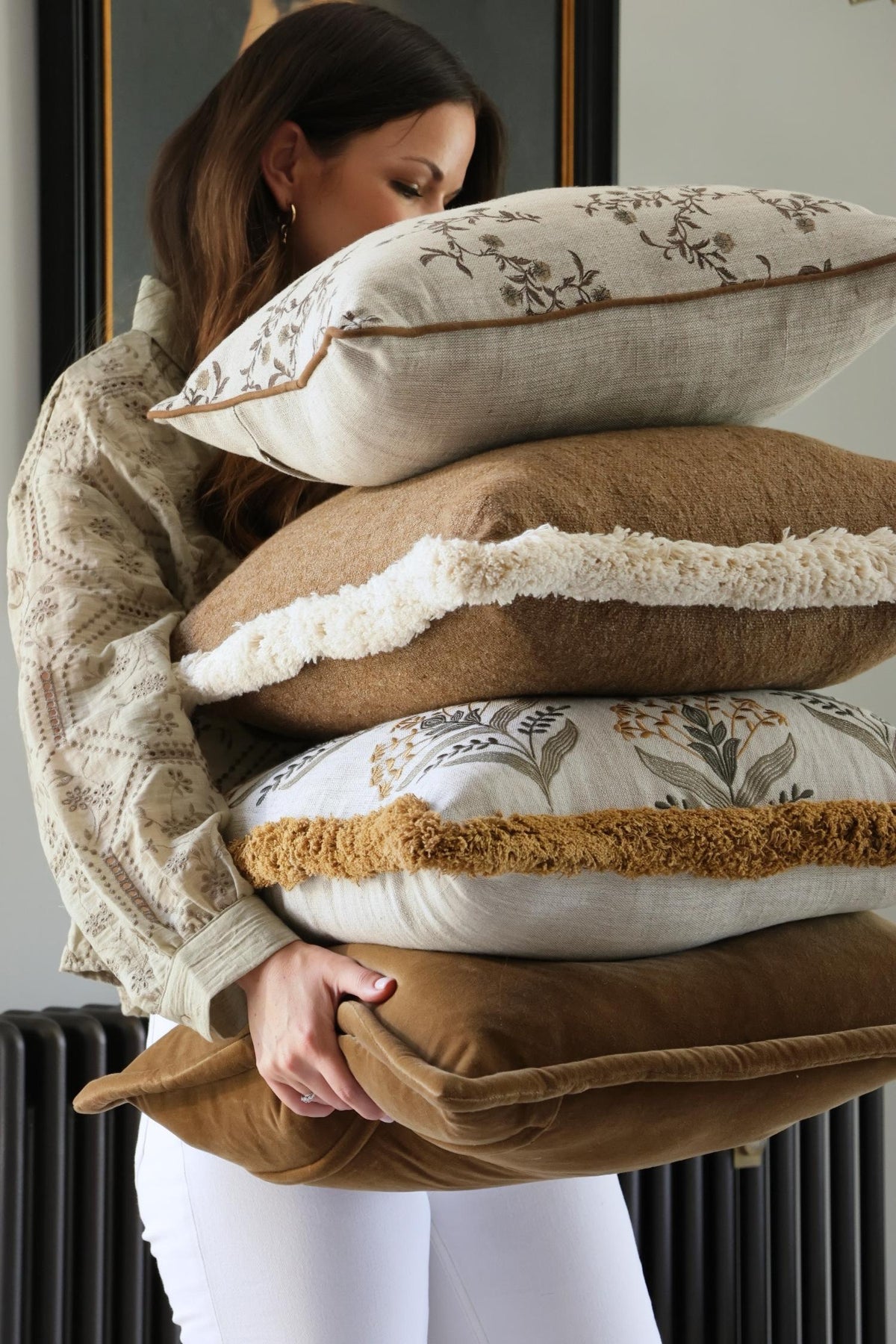 Woman holding a stack of decorative cushions with floral patterns.