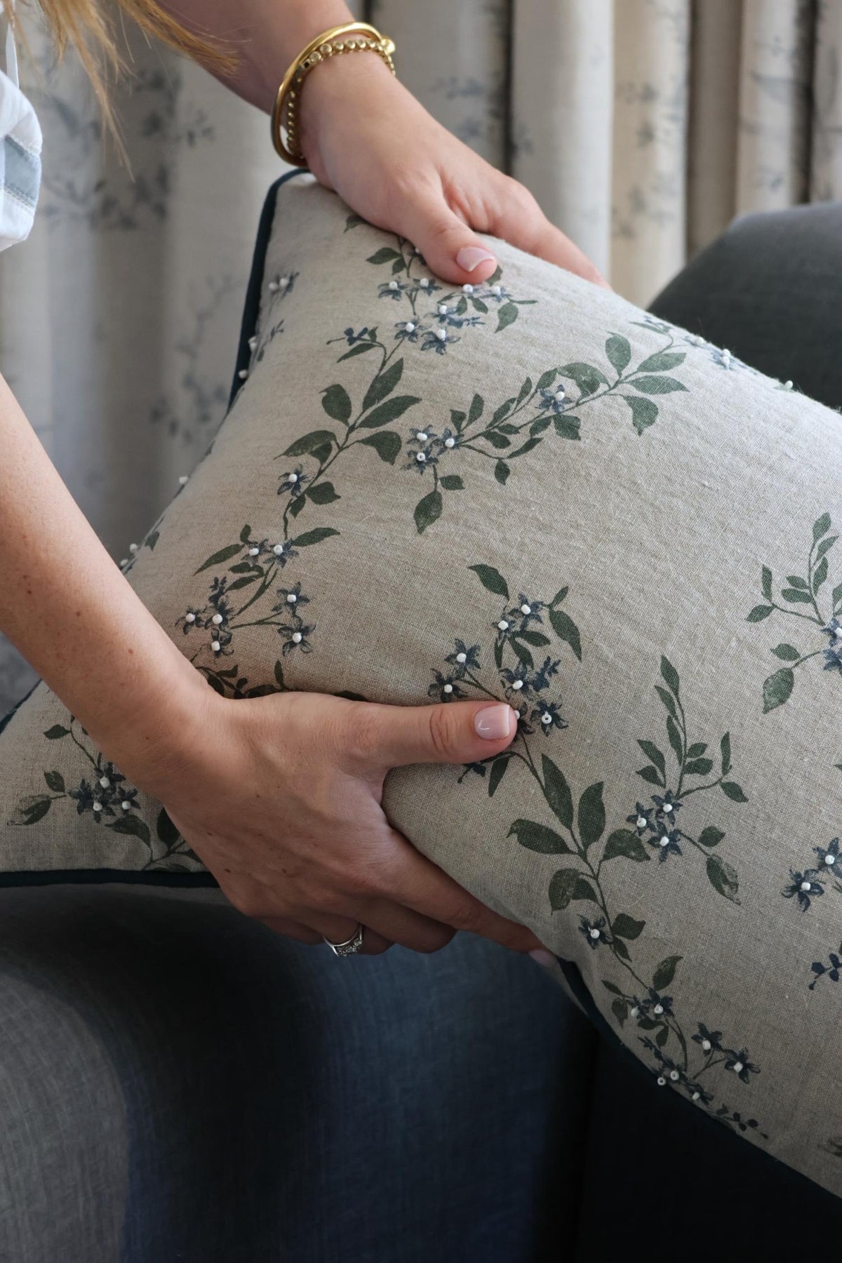 Person holding a floral-patterned cushion with green leaves and blue flowers with blue piping.