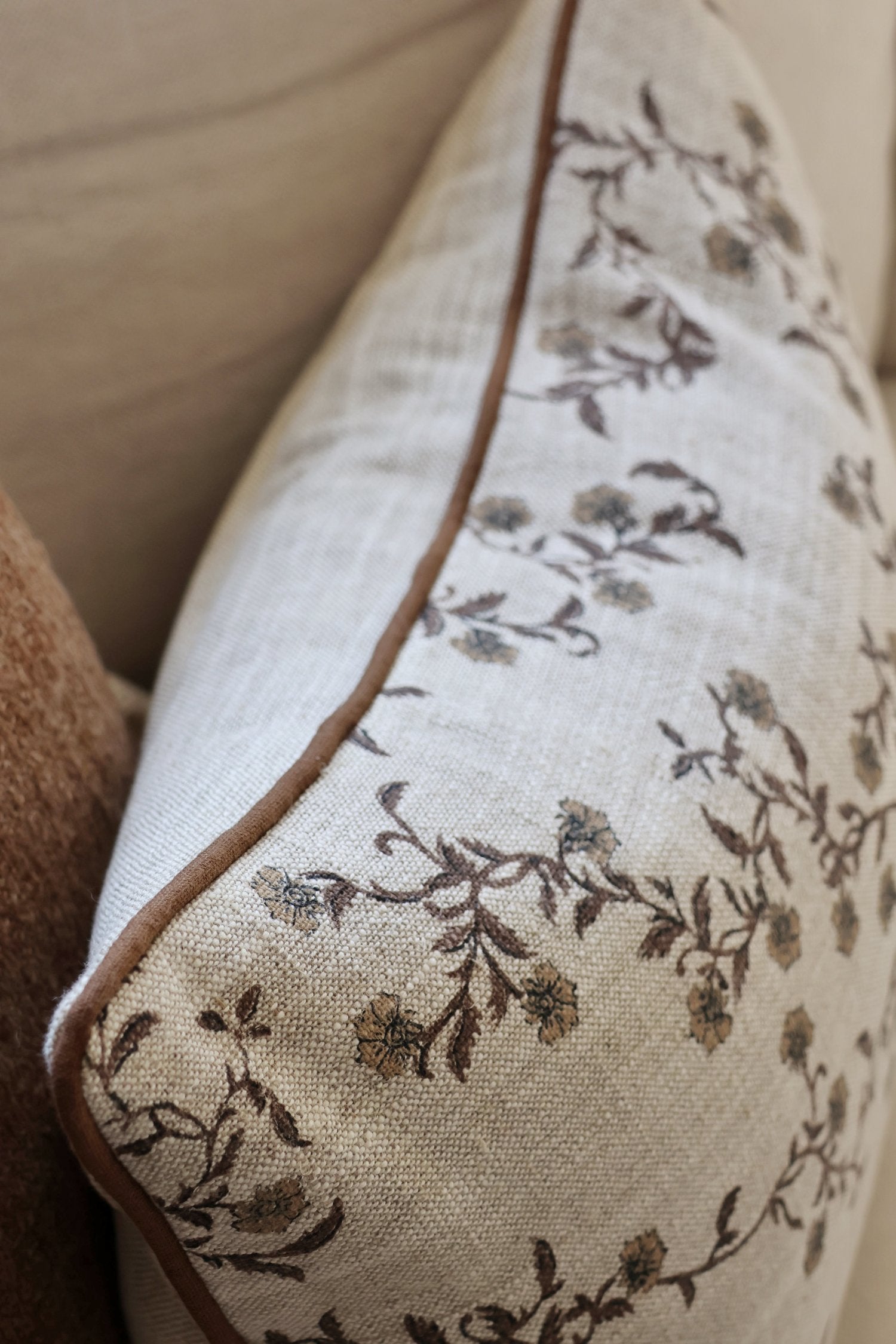 Floral patterned cushion with brown trim on a neutral background